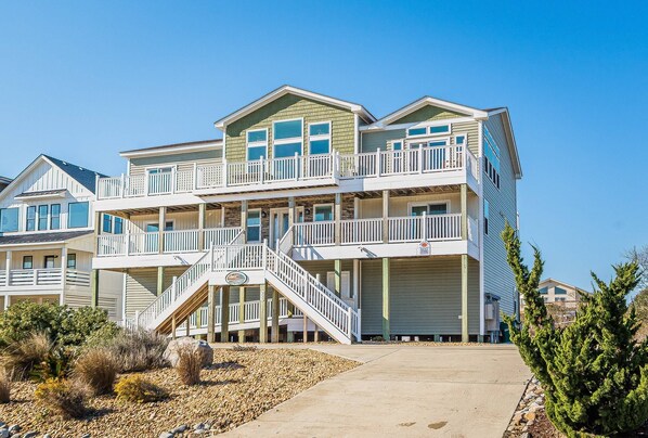 Una propiedad frente a la playa con varios pisos, balcones, una escalera central y vistas al mar.