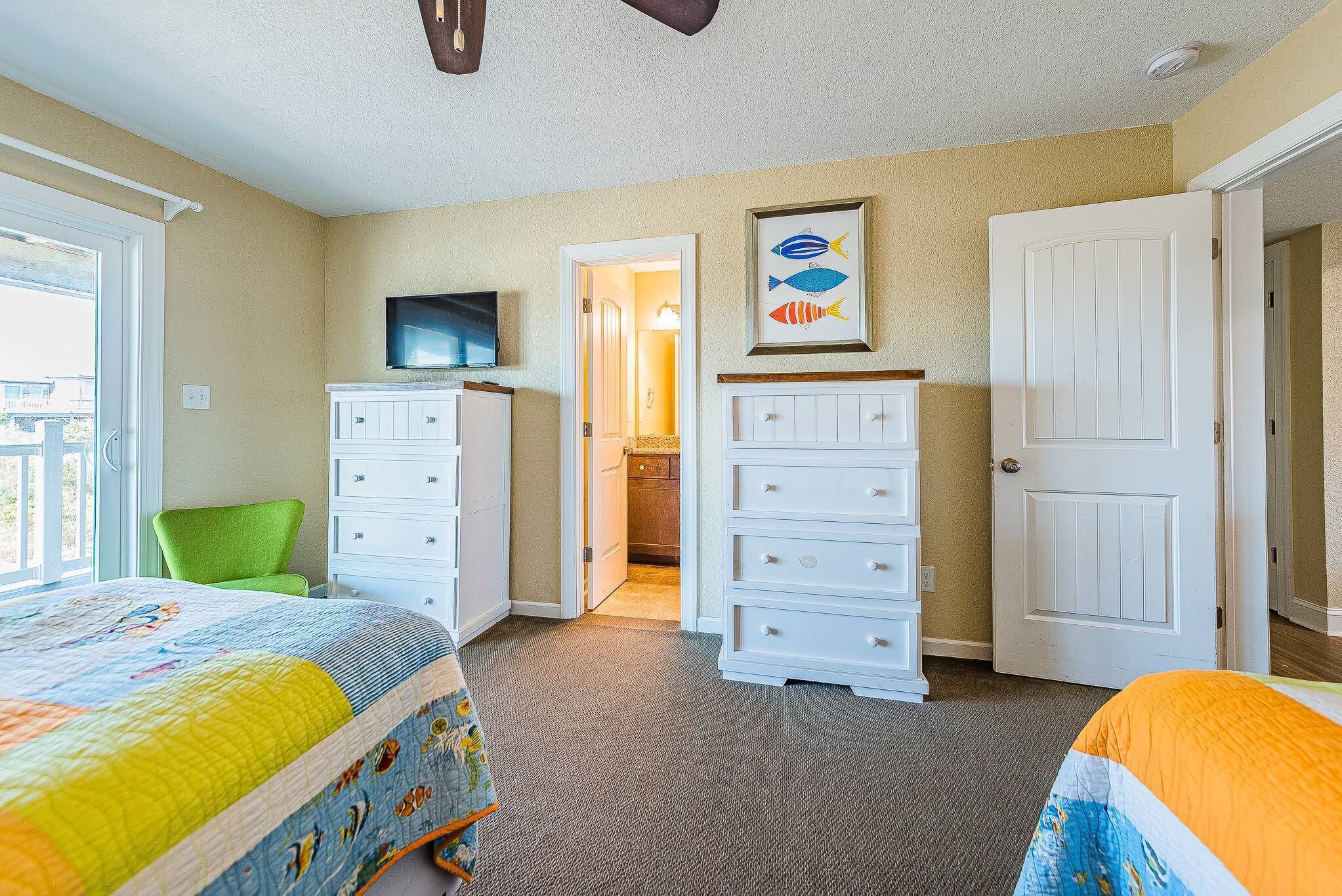 Un dormitorio con cama, cómoda, televisor y puerta que da a otra habitación.