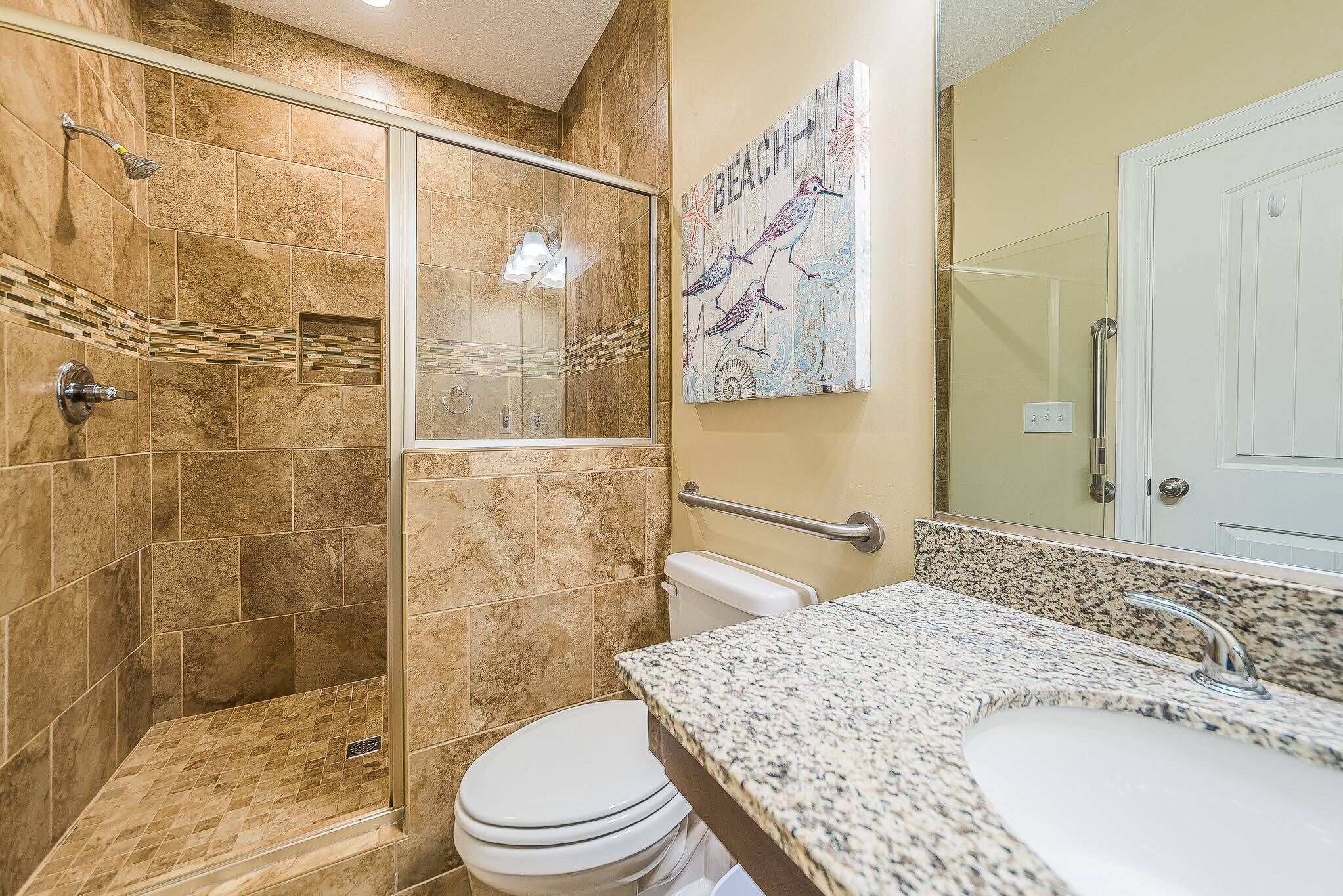 Bagno con cabina doccia in vetro, WC bianco e piano lavabo in granito.