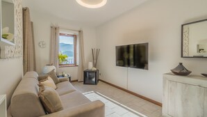 Ein modernes Wohnzimmer mit einer Couch, einem Fernseher, einem Schrank und einem Fenster mit Blick auf Berge.