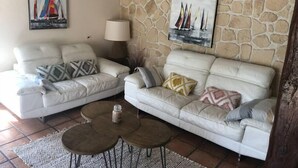 A living room with two white sofas, a stone wall, and two paintings of sailboats. - Le Cabanon (Portel-des-Corbières)