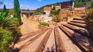 A stone staircase leading up to a building with a red roof, surrounded by greenery and a clear blue sky. - Le Cabanon (Portel-des-Corbières)