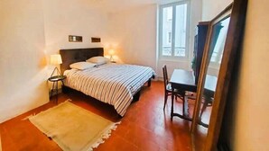 Un dormitorio con cama, lámparas de noche, una silla, una mesa y una ventana.