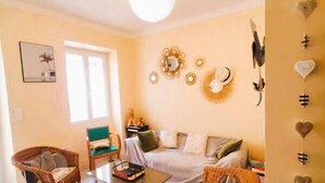 Una sala de estar acogedora con un sofá, dos sillones de mimbre, una mesita de centro y una estantería.