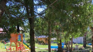 Ein Spielplatz mit Rutsche und Klettergerüsten, umgeben von Bäumen und Reifenplanzen.