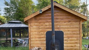 Eine Holzhütte mit Schornstein, einem Holzstapel und einem Metallofen.