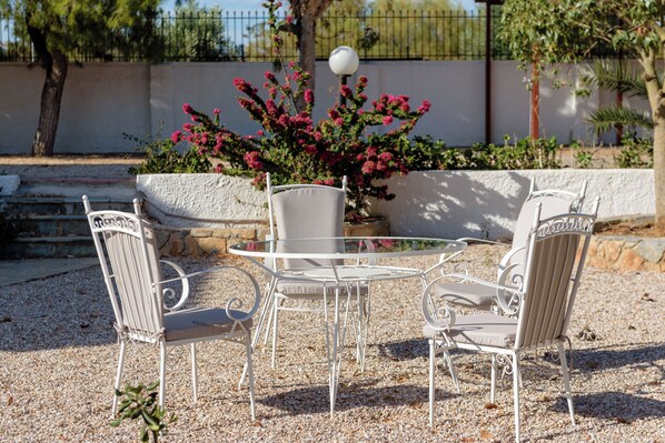 A round table with four white metal chairs, surrounded by pebbles. - Ktima EYzen (PXM7+665 Palea Fokea, Greece)