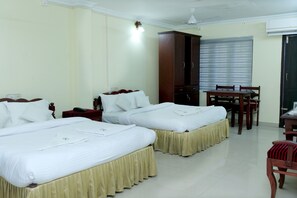 A hotel room with two beds, a wooden wardrobe, a dining table with chairs, and a ceiling fan. - Hotel Lumiere (Ambalapuzha)
