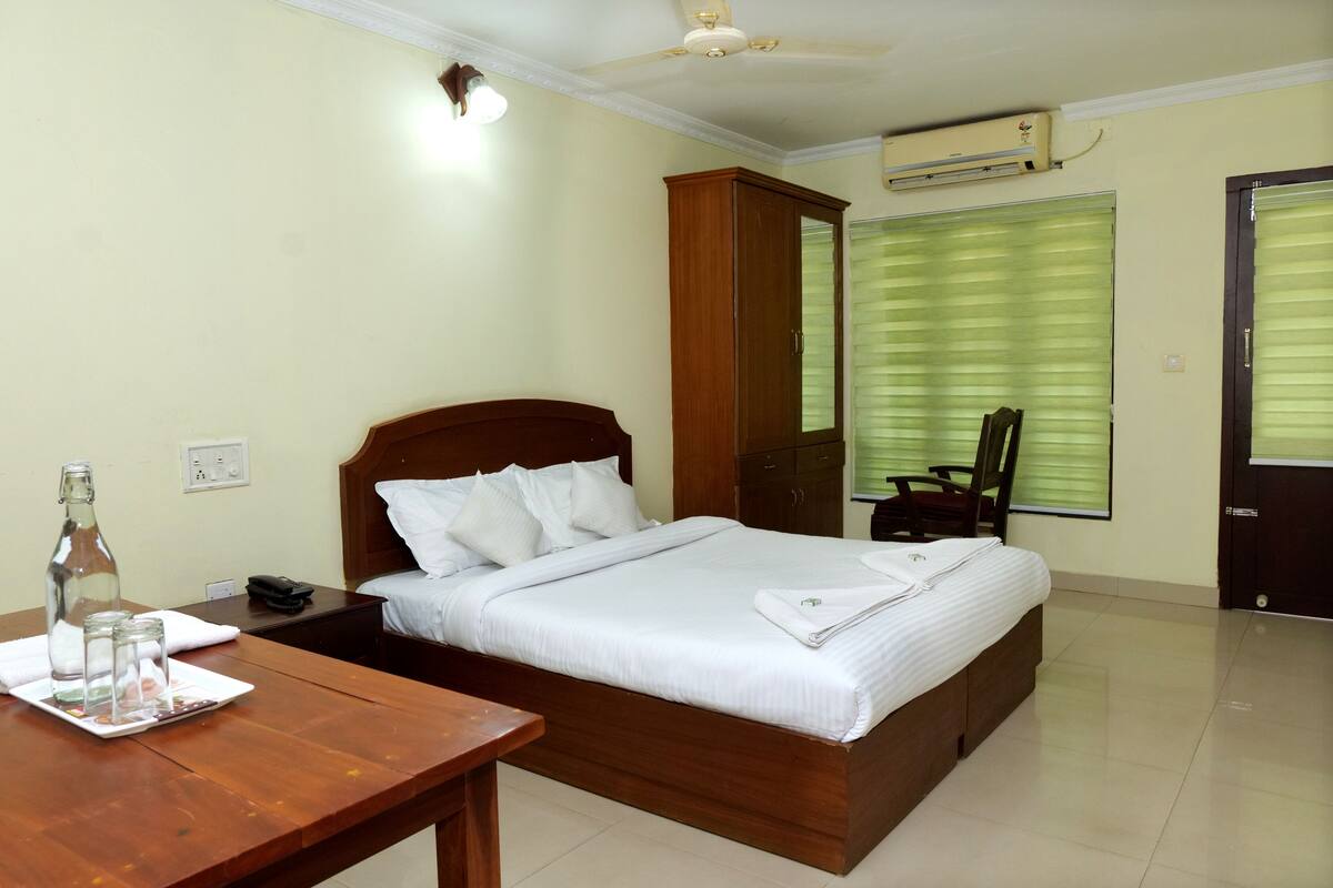 A neatly arranged bedroom with a wooden bed, a wooden nightstand, a table with a bottle and glasses, and a wardrobe.