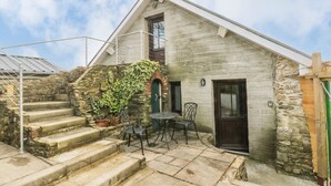 A stone building with a staircase leading to a door, a small outdoor seating area with two chairs, and a metal roof. - Green Grove Barn (Carmarthen)