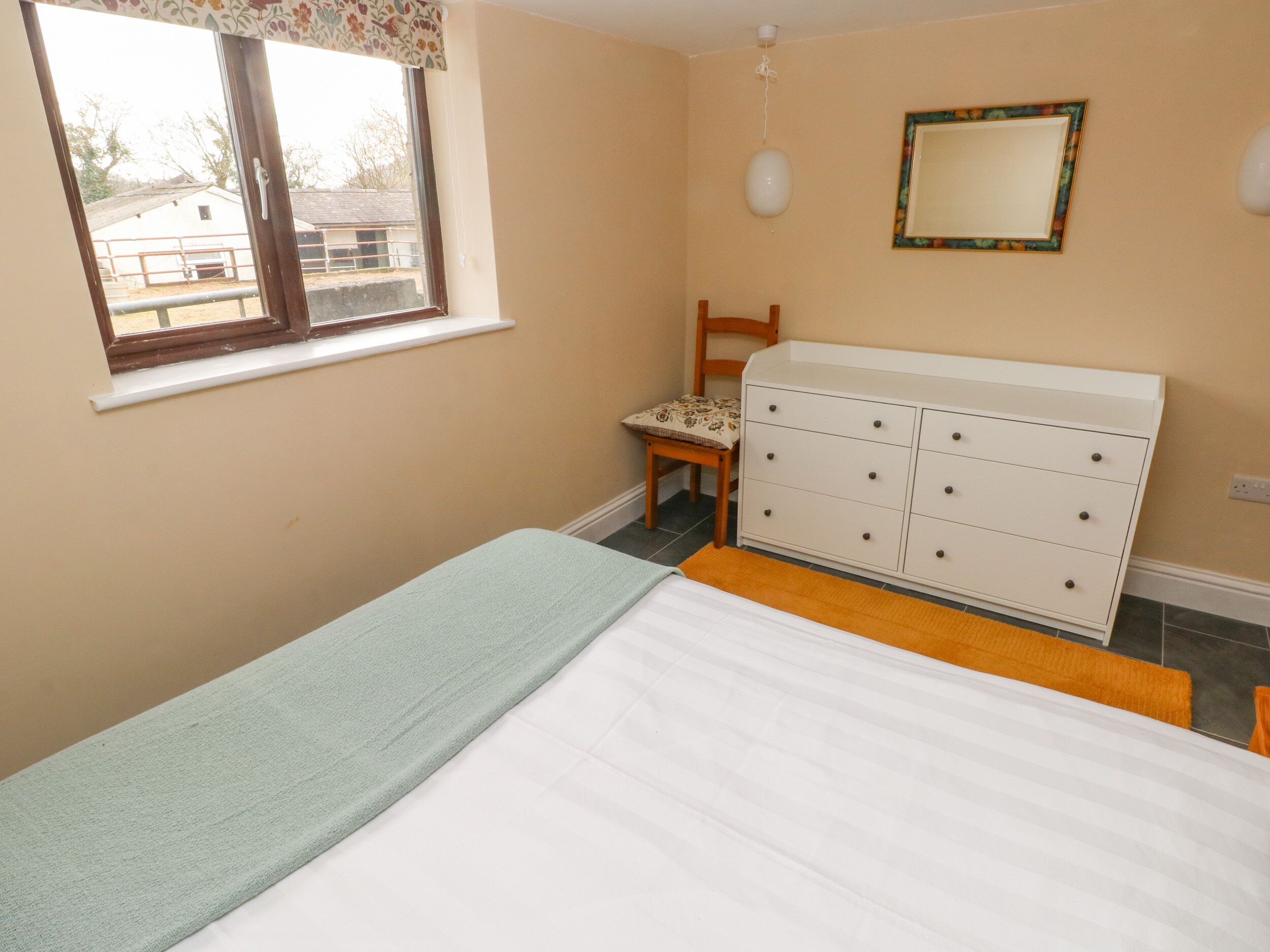 Un dormitorio con cama, cómoda, silla, ventana y espejo.