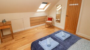A bedroom with a sloped ceiling, a skylight, a wooden wardrobe, a chair, a bed with towels, and a small table. - Green Grove Barn (Carmarthen)