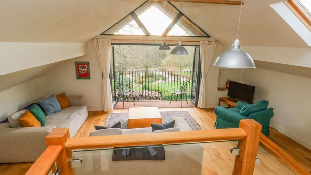 A spacious loft apartment with a high ceiling, wooden flooring, and a balcony with a view of the garden. - Green Grove Barn (Carmarthen)