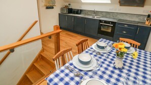 A modern kitchen with dark cabinets, a skylight, and a dining area with a blue and white checkered tablecloth. - Green Grove Barn (Carmarthen)