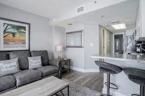 A modern living room with a grey sofa, a coffee table, and a framed picture of a beach scene. - Beautiful Oceanfront 1 Bedroom Condo at Seawatch Resort (Myrtle Beach)