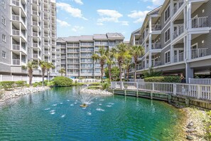 A multi-story hotel with balconies, a central courtyard with a fountain, and a small bridge. - Beautiful Oceanfront 1 Bedroom Condo at Seawatch Resort (Myrtle Beach)