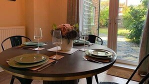 Ein runder Esstisch ist gedeckt mit Tellern, Weingläsern und einer Blumenvase.