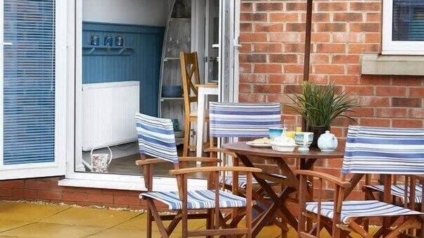 An outdoor patio with a table and chairs, a striped umbrella, and a brick wall. - The Nets - Fantastic 3 bedroom house with parking (Filey)