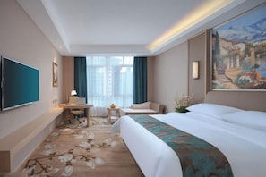 A hotel room with a bed, a desk, a chair, a TV, and a painting on the wall. - Changtai Jinbang International Hotel (Zhangzhou)