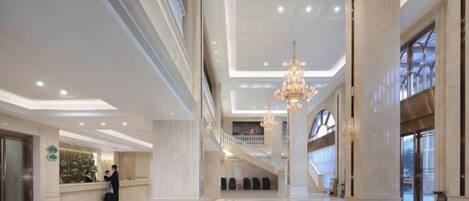 A spacious lobby with a grand staircase, a reception desk, and a chandelier.
