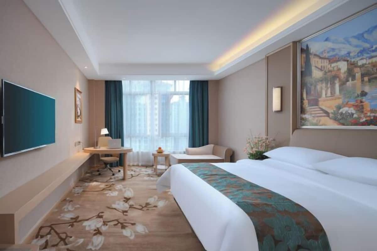 A hotel room with a bed, desk, chair, TV, and a painting on the wall.