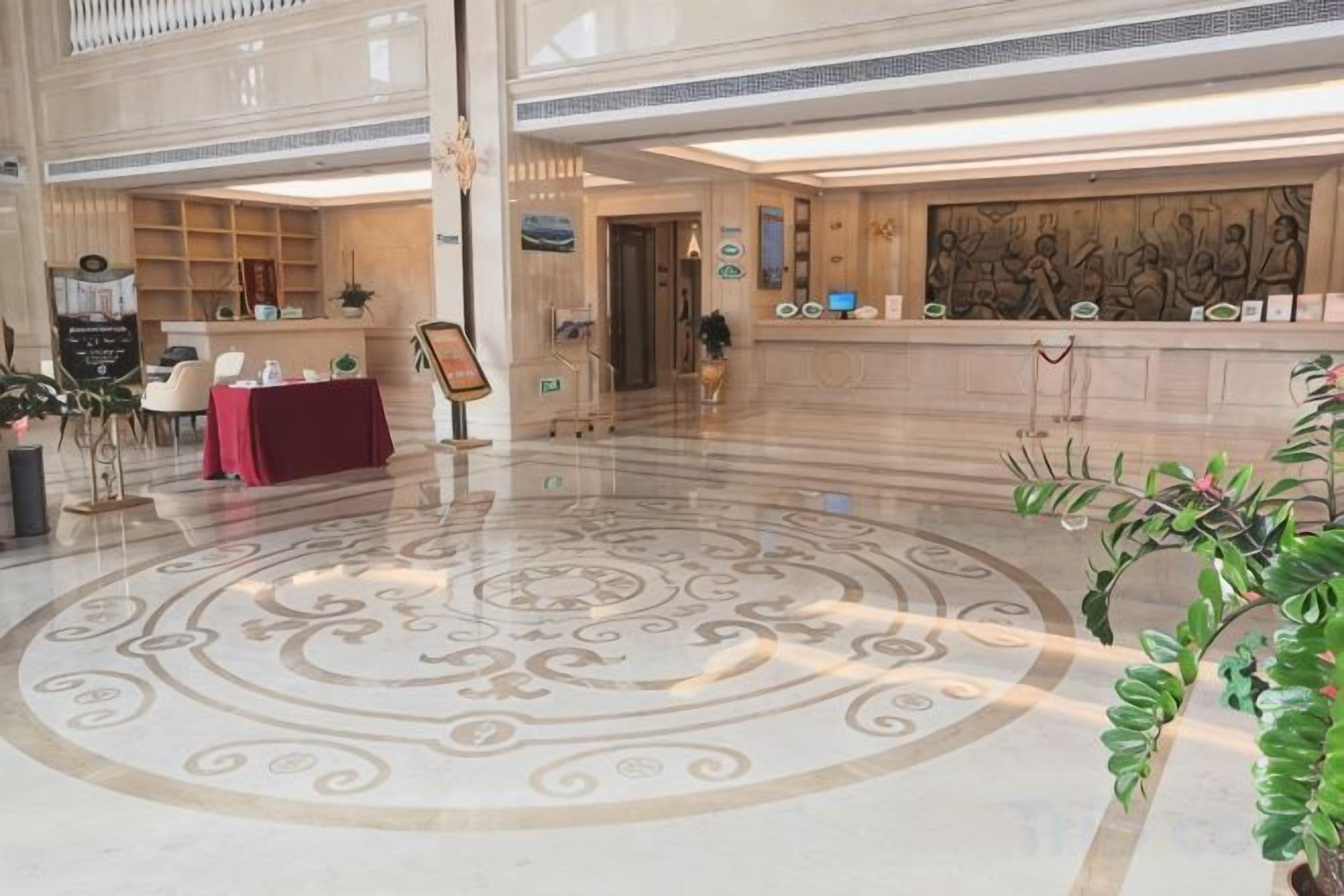 Eine Lobby mit einem zentralen, kreisförmigen Bodenmuster, einem Empfangstresen und einer Sitzecke mit rotem Tischlein.