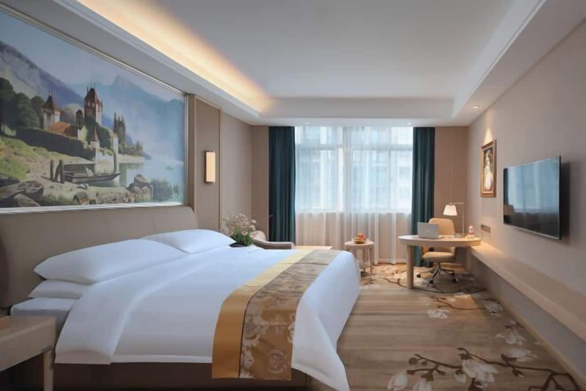A hotel room with a large bed, a desk, a chair, a TV, and a painting on the wall.