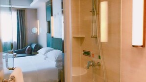 A hotel room with a bed, a glass partition, a shower with a handheld showerhead, and a wall-mounted light. - Changtai Jinbang International Hotel (Zhangzhou)