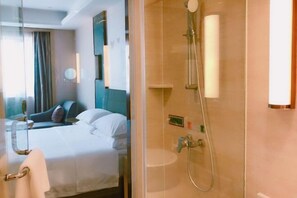 A hotel room with a bed, a glass partition, a shower with a handheld showerhead, and a wall-mounted light. - Changtai Jinbang International Hotel (Zhangzhou)