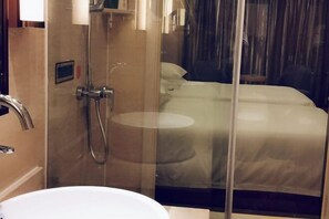 A bathroom with a sink, shower, and a bed with a glass partition. - Changtai Jinbang International Hotel (Zhangzhou)