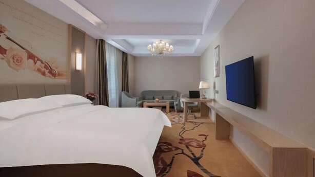 A hotel room with a bed, a desk with a computer, a television, and a chandelier. - Changtai Jinbang International Hotel (Zhangzhou)