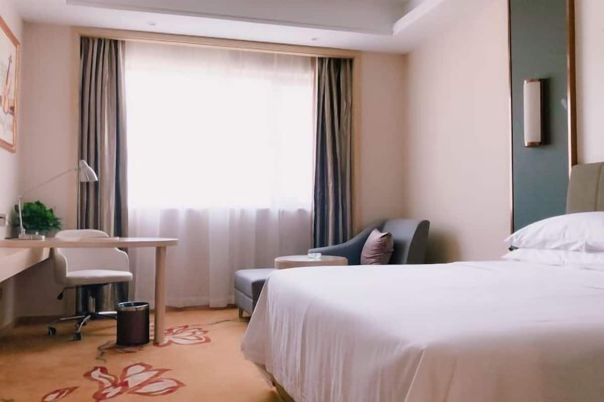 A hotel room with a bed, desk, chair, and a window with curtains.