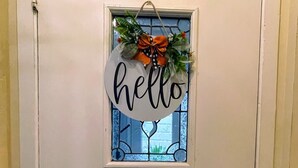 Une porte blanche avec une petite fenêtre, une pancarte indiquant « Bonjour » et un sonnette.