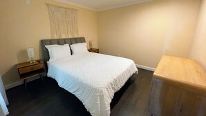 Une chambre à coucher avec un grand lit, deux tables de chevet, une petite table, un banc en bois et un luminaire fixé au mur.