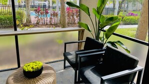 A balcony with a view of a landscaped garden, featuring a white fence, palm trees, and various plants. - Oasis Resort Style Condo 2/2 (Naples)