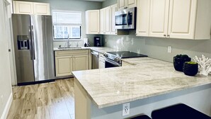 A modern kitchen with a large island, stainless steel appliances, and light-colored cabinetry. - Oasis Resort Style Condo 2/2 (Naples)