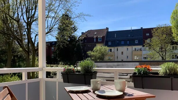 Une terrasse extérieure avec une table et des chaises en bois, entourée de jardinières fleuries.