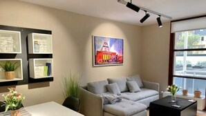 Un salon moderne avec un canapé d’angle gris, une table basse noire et un tableau accroché au mur. On y trouve également une table à manger avec des chaises et un vase rempli de fleurs.