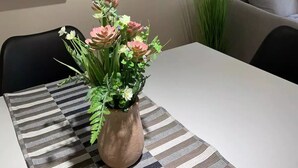 Un coin repas avec une table dressée pour deux personnes, un vase rempli de fleurs et des étagères murales où sont disposés divers objets.