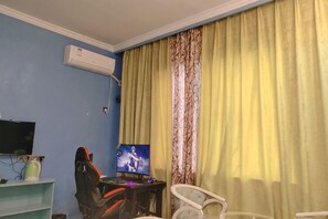 Ein Zimmer mit Schreibtisch, Stuhl, Fernseher und einem Fenster mit Vorhängen.
