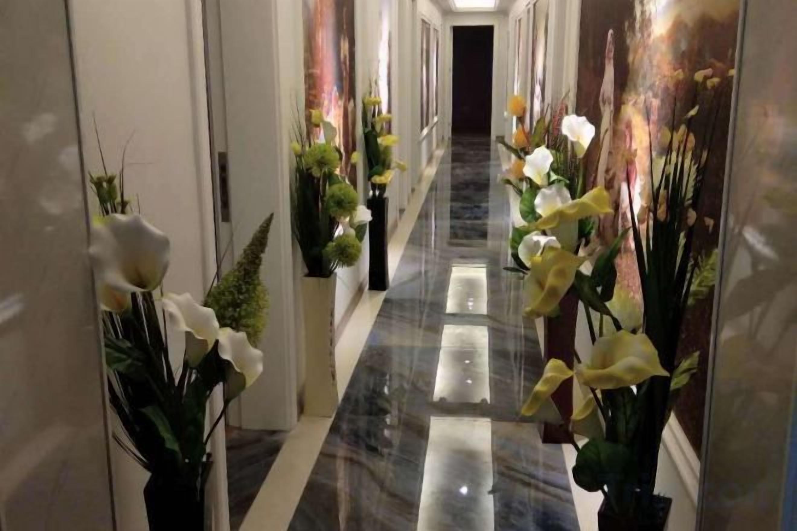 A hallway with a marble floor, potted plants, and framed artwork on the walls.