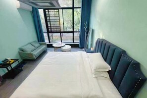 A hotel room with a bed, a sofa, a small round table, and a window with curtains. - Lvsenlingongyu (Chenzhou)