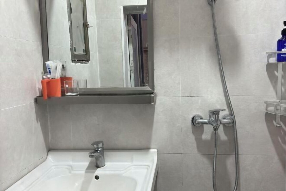 A bathroom with a sink, mirror, shower, and a shelf with toiletries.