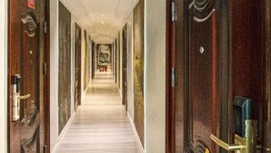 Un couloir d’hôtel avec des portes des deux côtés, un sol recouvert de moquette et, au bout, une vue sur le hall d’entrée.