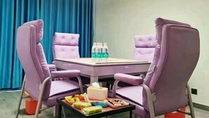 Une pièce avec une table violette et des chaises assorties, une petite table avec des collations et des boissons, et un rideau bleu en arrière-plan.
