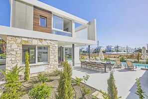 Una casa moderna de dos pisos con fachada de piedra, un balcón y un área de piscina con mobiliario exterior.