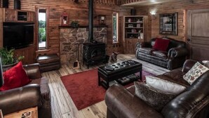 Een rustiek houten interieur met een stenen openhaard, leren banken, een televisie en houten wanden.