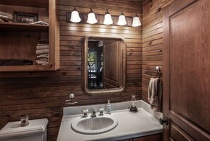 Une salle de bain aux murs lambrissés, avec un lavabo blanc, un miroir et un porte-serviettes.