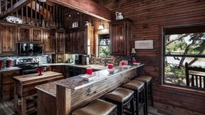 Een landelijke keuken met houten kastjes, een granieten aanrecht en een bar met krukken.