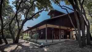 Een rustiek houten gebouw met een overdekte veranda en grote ramen, omringd door bomen.